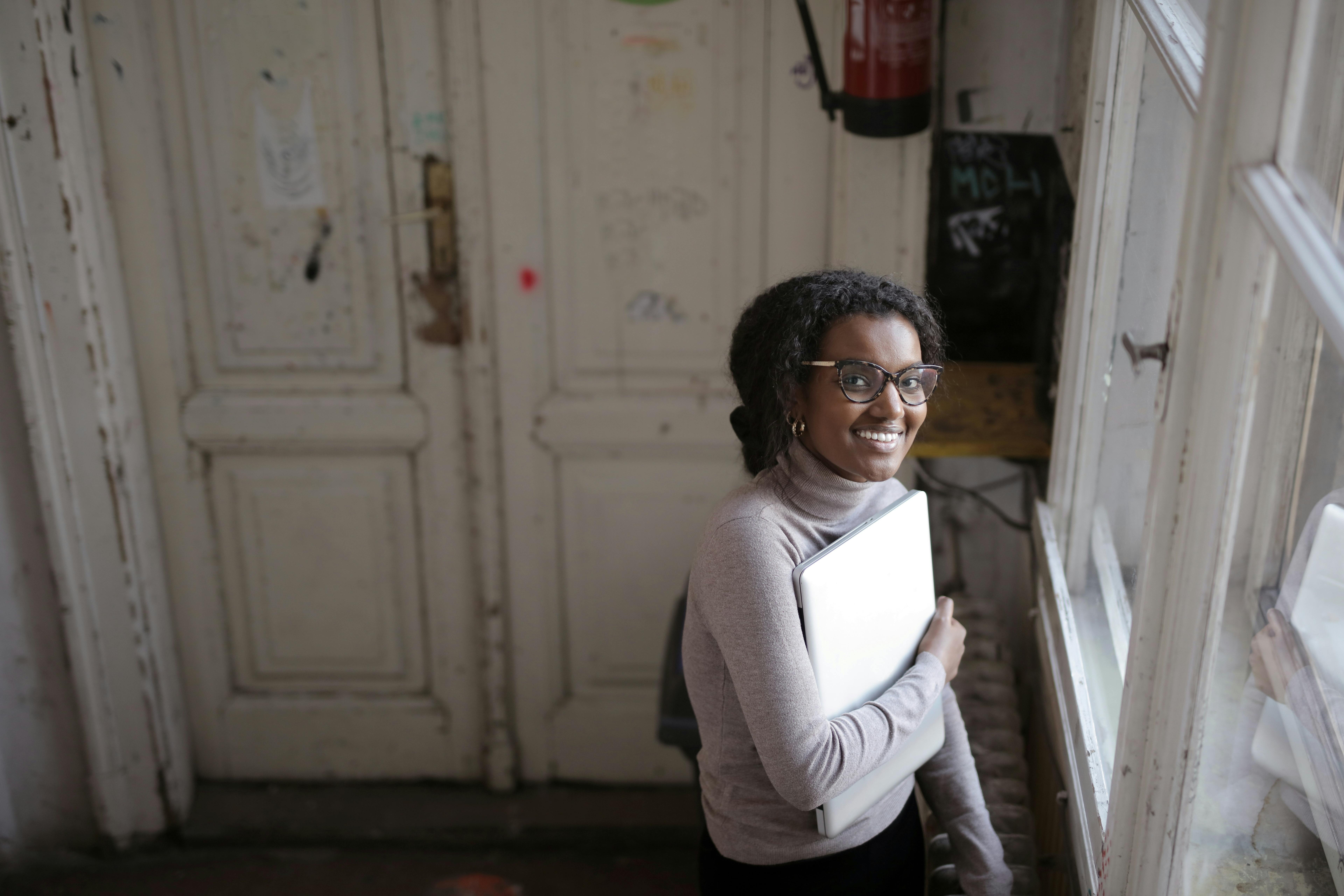 Smiling woman holding laptop in vintage room with rustic doors. Perfect for business or study concepts.