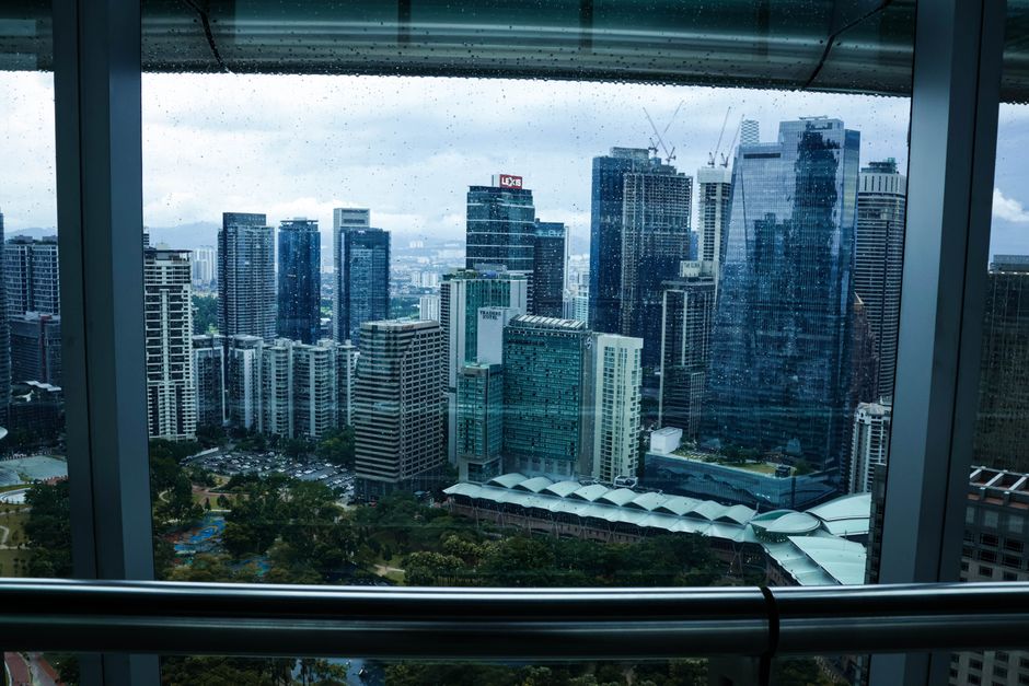 Overcast view of Kuala Lumpur's modern skyline through a rain-speckled window.