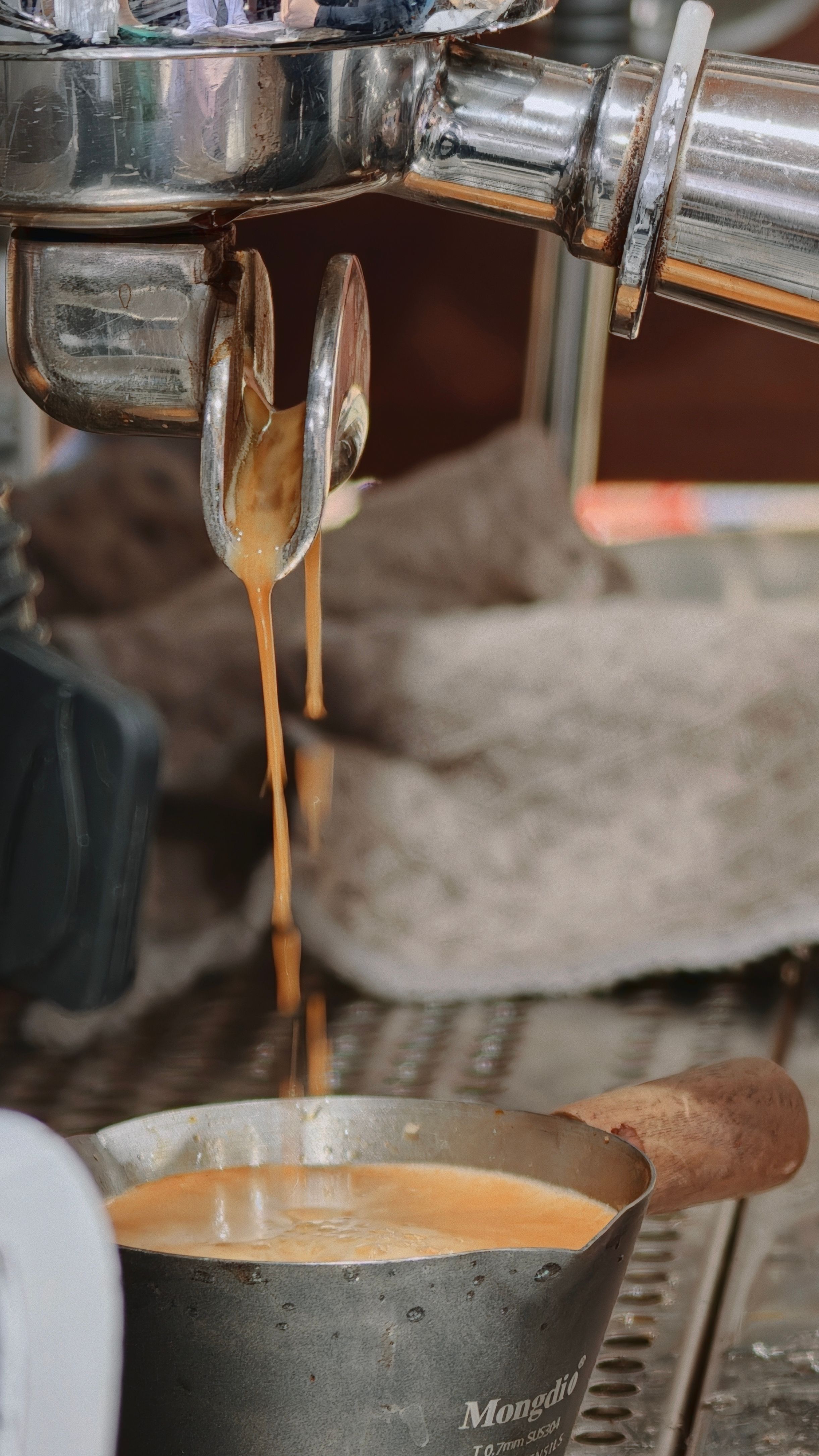 Close-up of espresso pouring from a machine into a metal jug at a café.