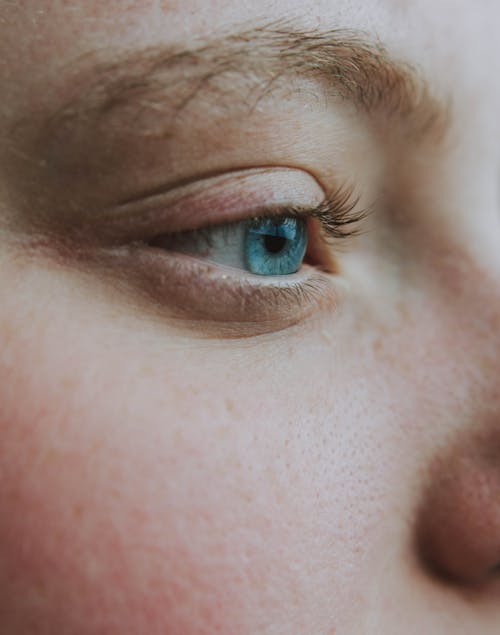 Closeup side view of crop anonymous wistful female looking away with turquoise eye and black eyelashes with brown eyebrows and pores on face skin