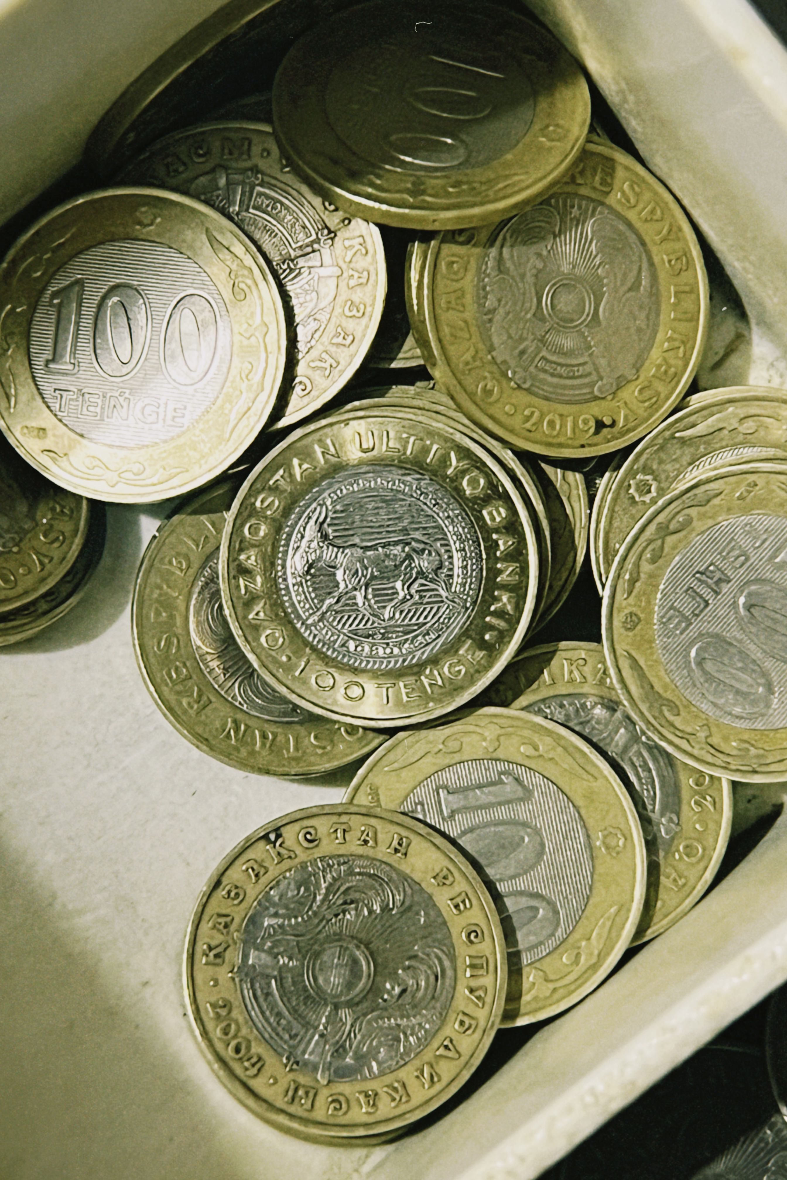 Close-up image of Kazakhstani tenge coins in a container, showcasing currency details.