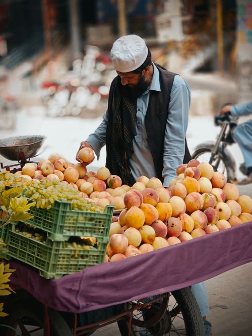 Free A street vendor arranges fresh peaches on a cart in a bustling outdoor market. Vivid lifestyle scene. Stock Photo