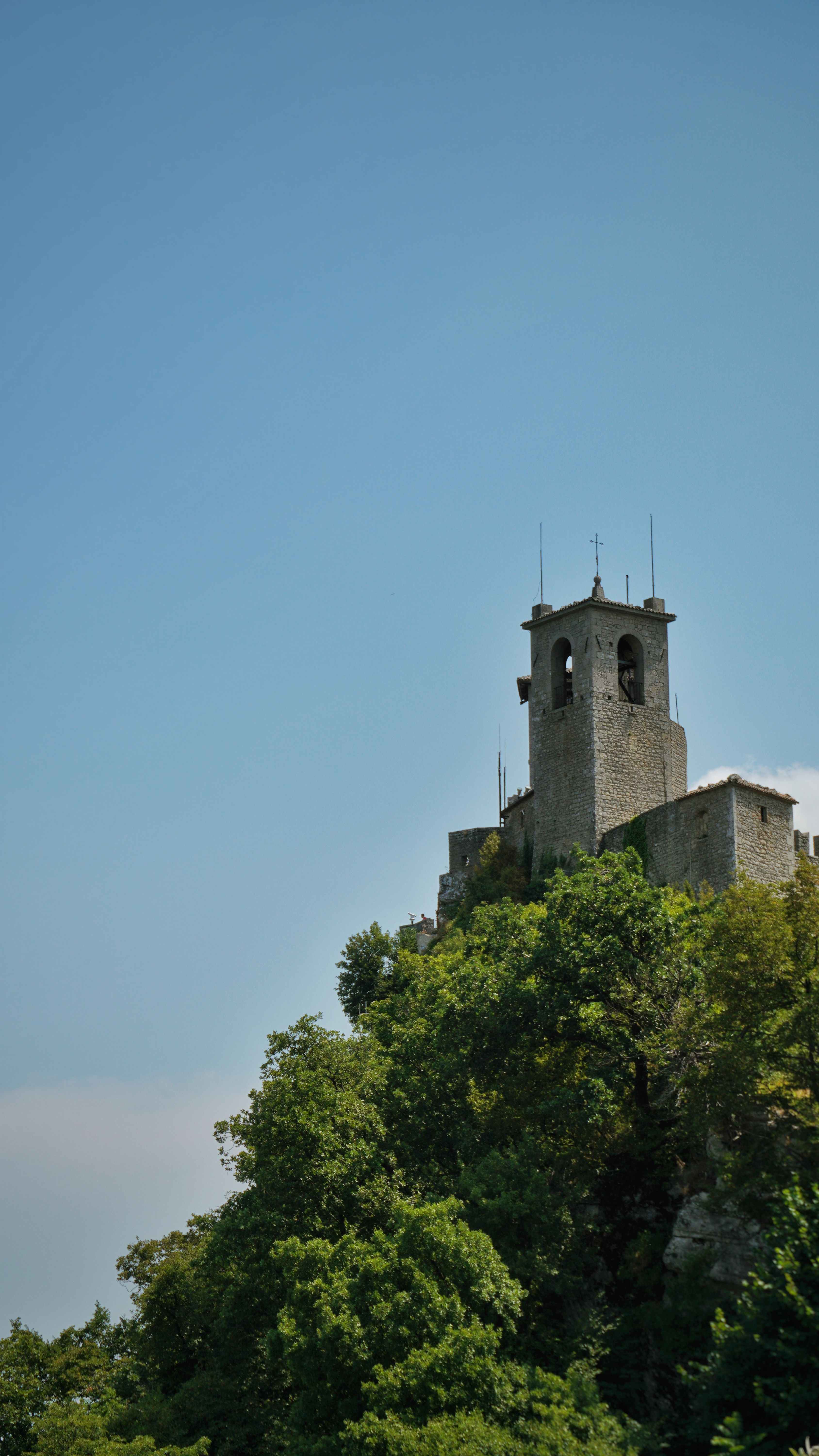 Scenic view of an ancient stone tower atop a green hill in San Marino against a blue sky.