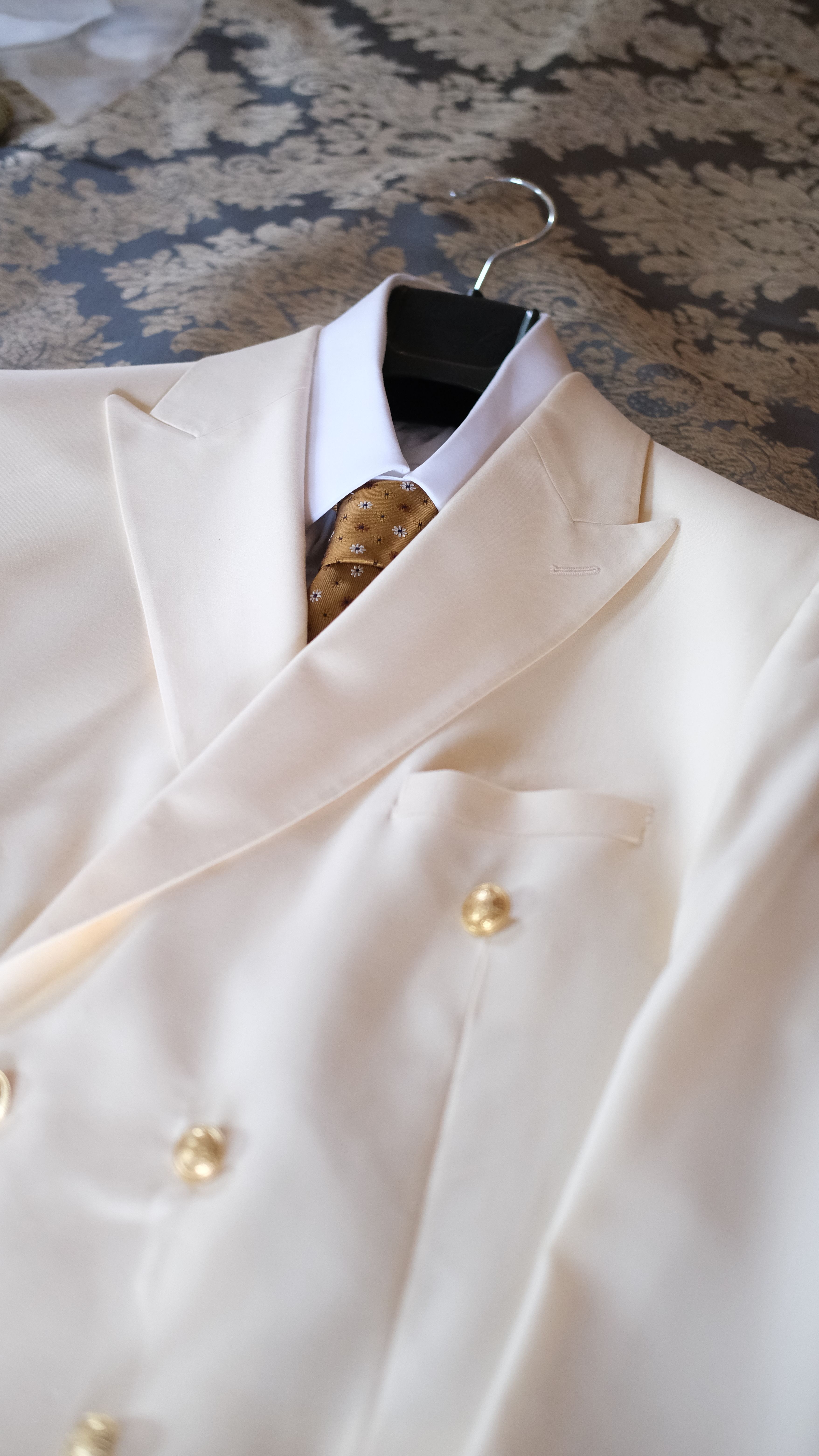 A close-up shot of a stylish cream suit and gold tie on a hanger, perfect for formal occasions.
