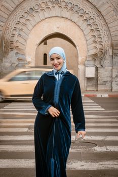 Woman in a blue djellaba with a hijab stands confidently in Marrakesh, Morocco.