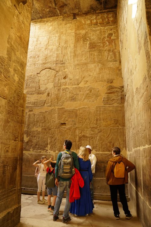 Free A group of tourists admires the engravings on ancient Egyptian temple walls, showcasing detailed hieroglyphics. Stock Photo