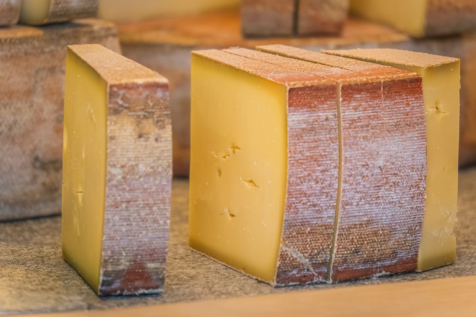 A wedge of aged Gruyère cheese with its natural brown rind, cut open to show the pale yellow interior with small scattered holes.