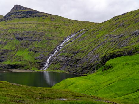Beautiful waterfall cascading down a lush, green hillside into a serene lake.