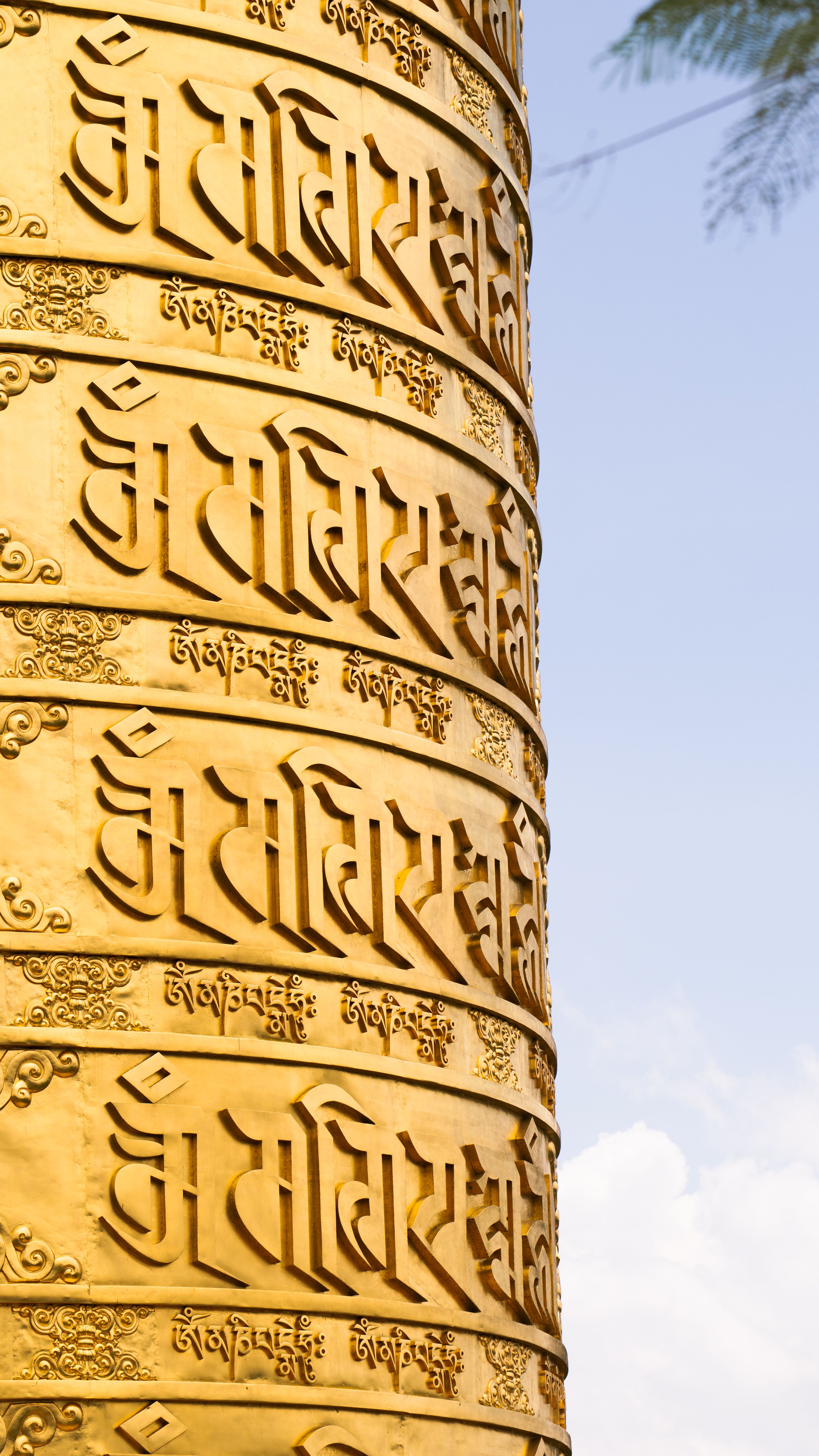 Close-up of a golden prayer wheel featuring intricate Tibetan script under a clear sky in Da Lat, Vietnam.