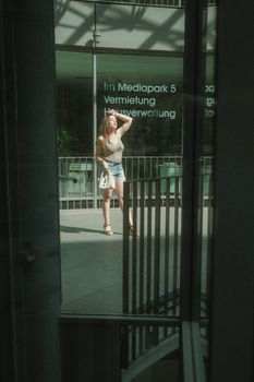 A young woman poses stylishly in the sunlit Mediapark, Cologne, Germany.