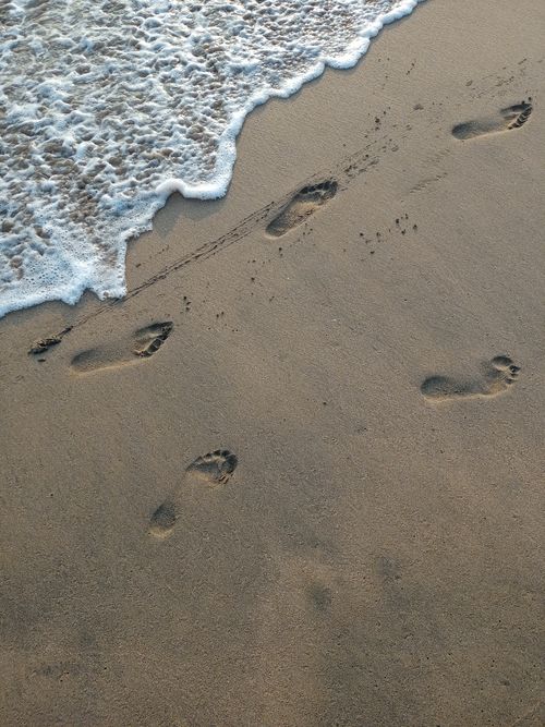 Free Footprints in wet sand near ocean waves create a serene coastal scene. Stock Photo