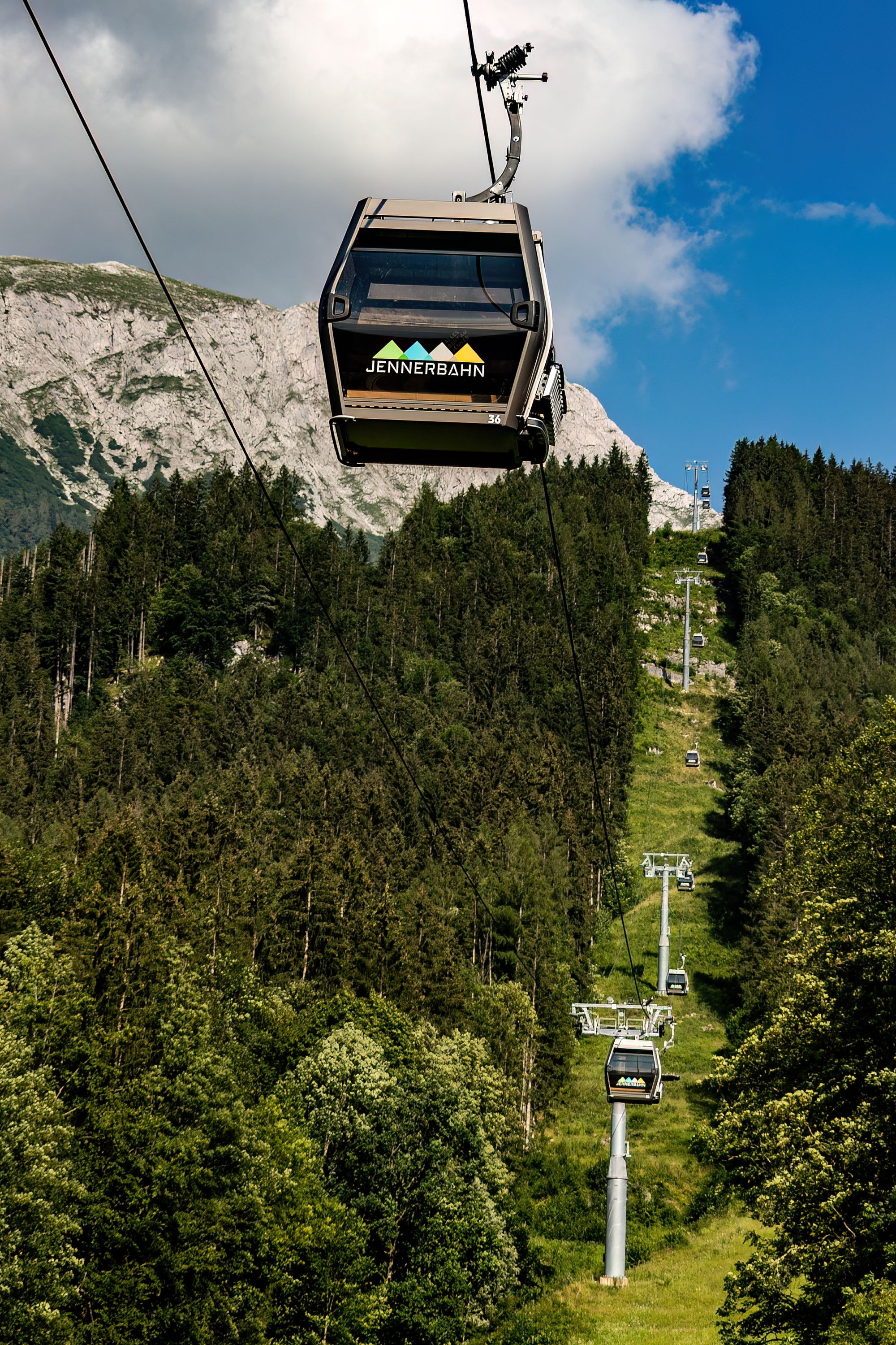 Scenic view of Jennerbahn cable car climbing through lush forests of Schönau am Königssee, Bavaria.