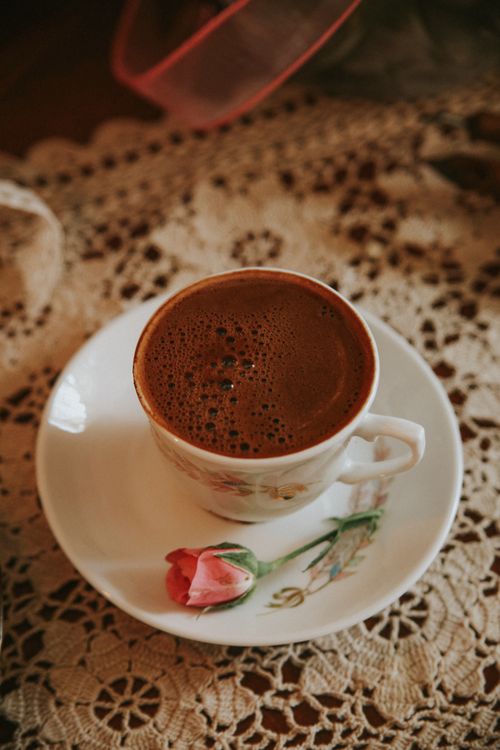 Free A beautifully crafted coffee cup on a lace tablecloth with a single pink flower. Stock Photo