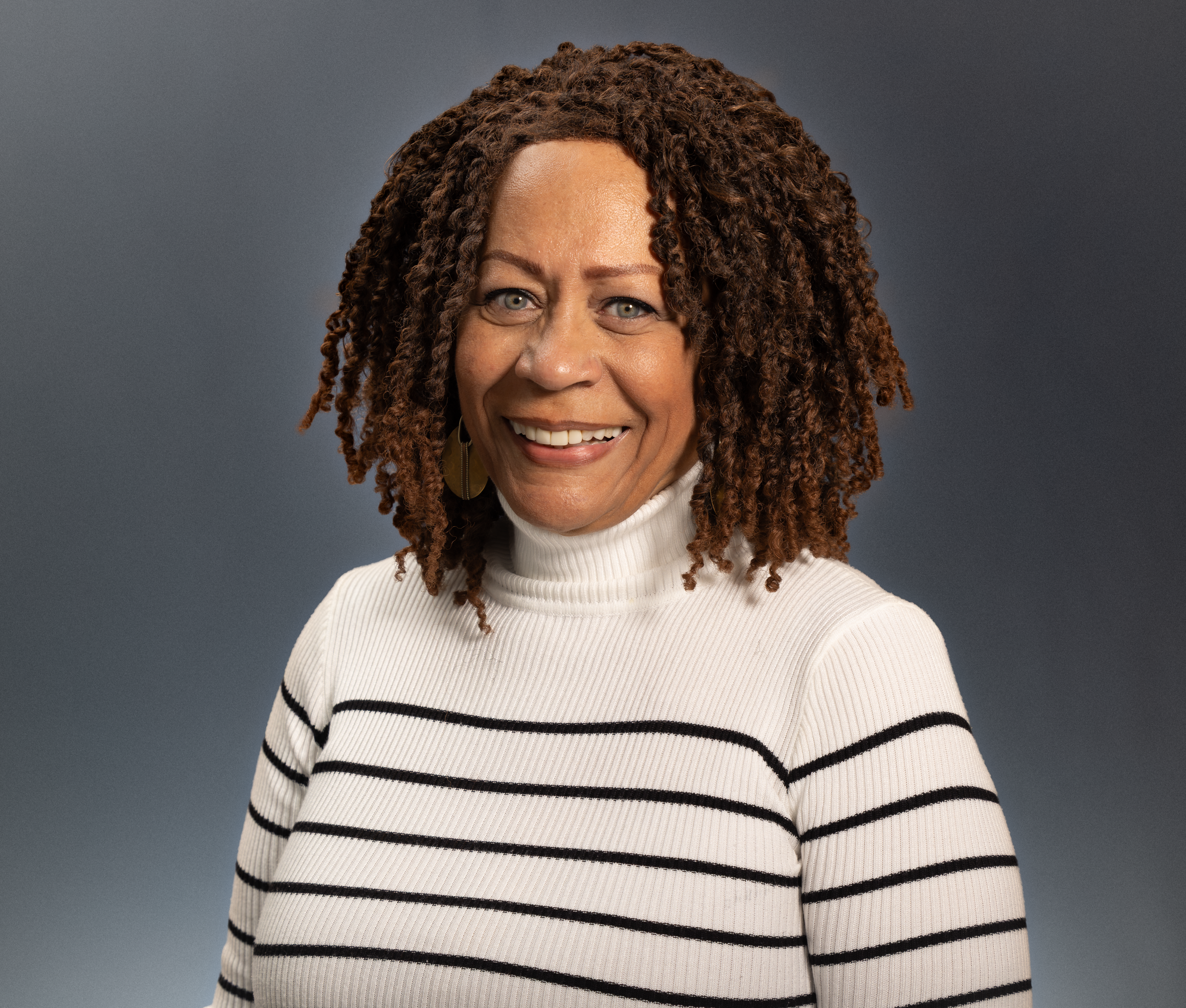 Portrait of a smiling woman wearing a white and black striped sweater against a grey backdrop.
