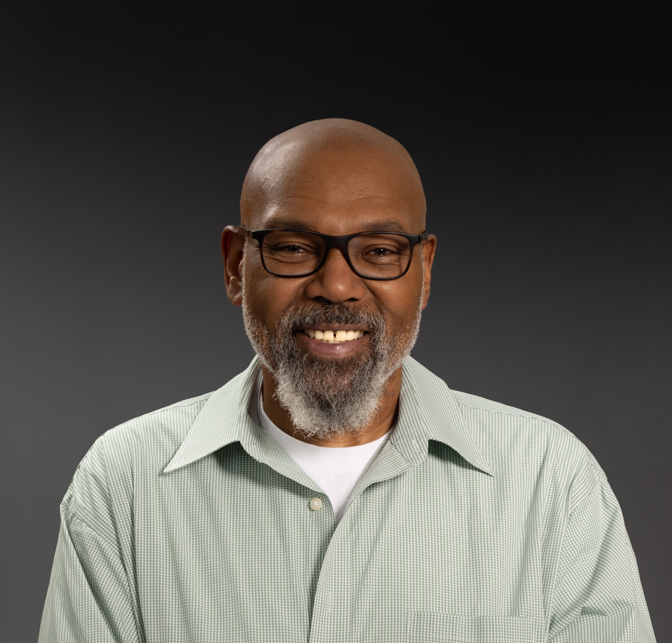 Smiling mature man wearing glasses and green shirt, friendly expression.