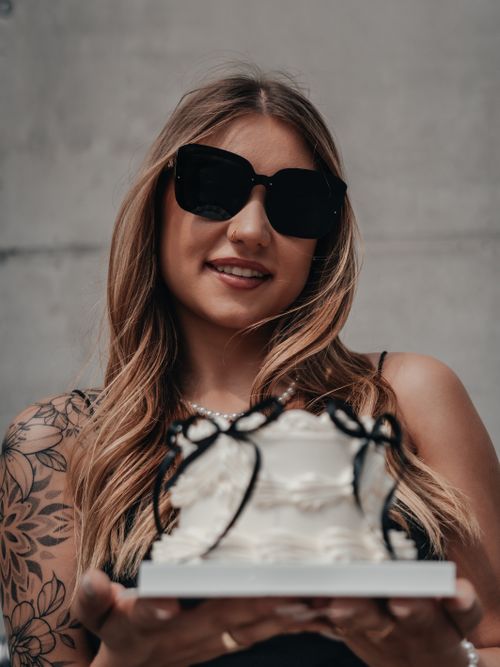 Free Stylish woman with sunglasses and tattoo holding a birthday cake in an elegant setting. Stock Photo
