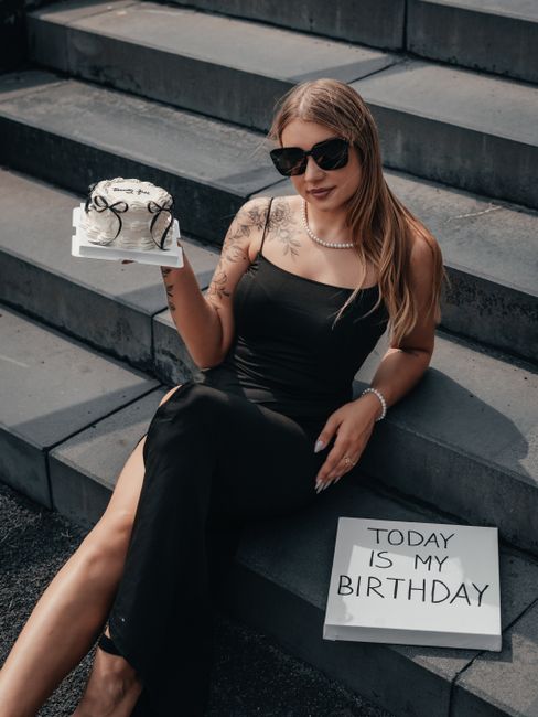Young woman in a black dress celebrating her birthday with a cake outdoors.