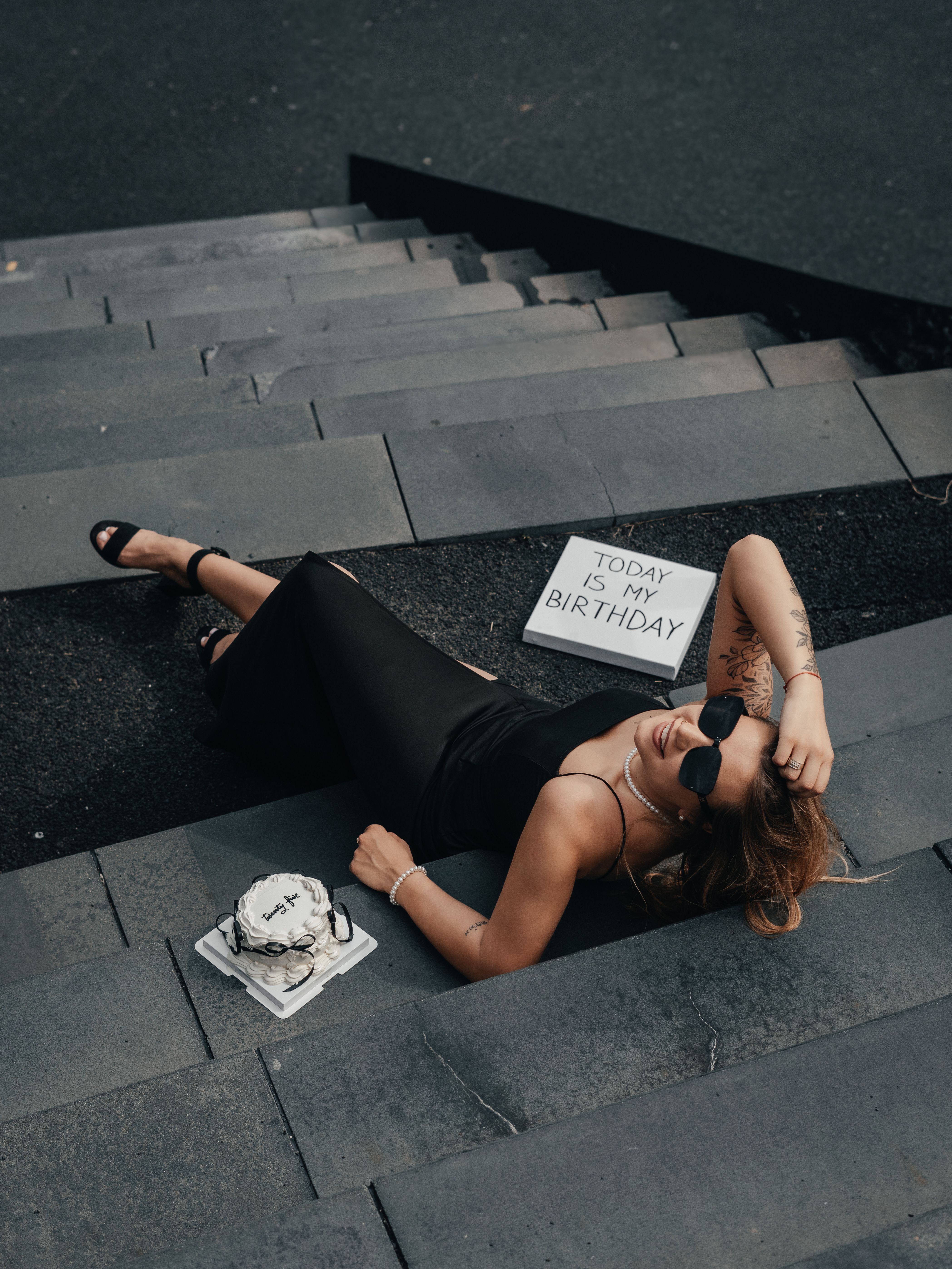 Elegant woman celebrating her birthday on city steps with a cake and stylish decor.