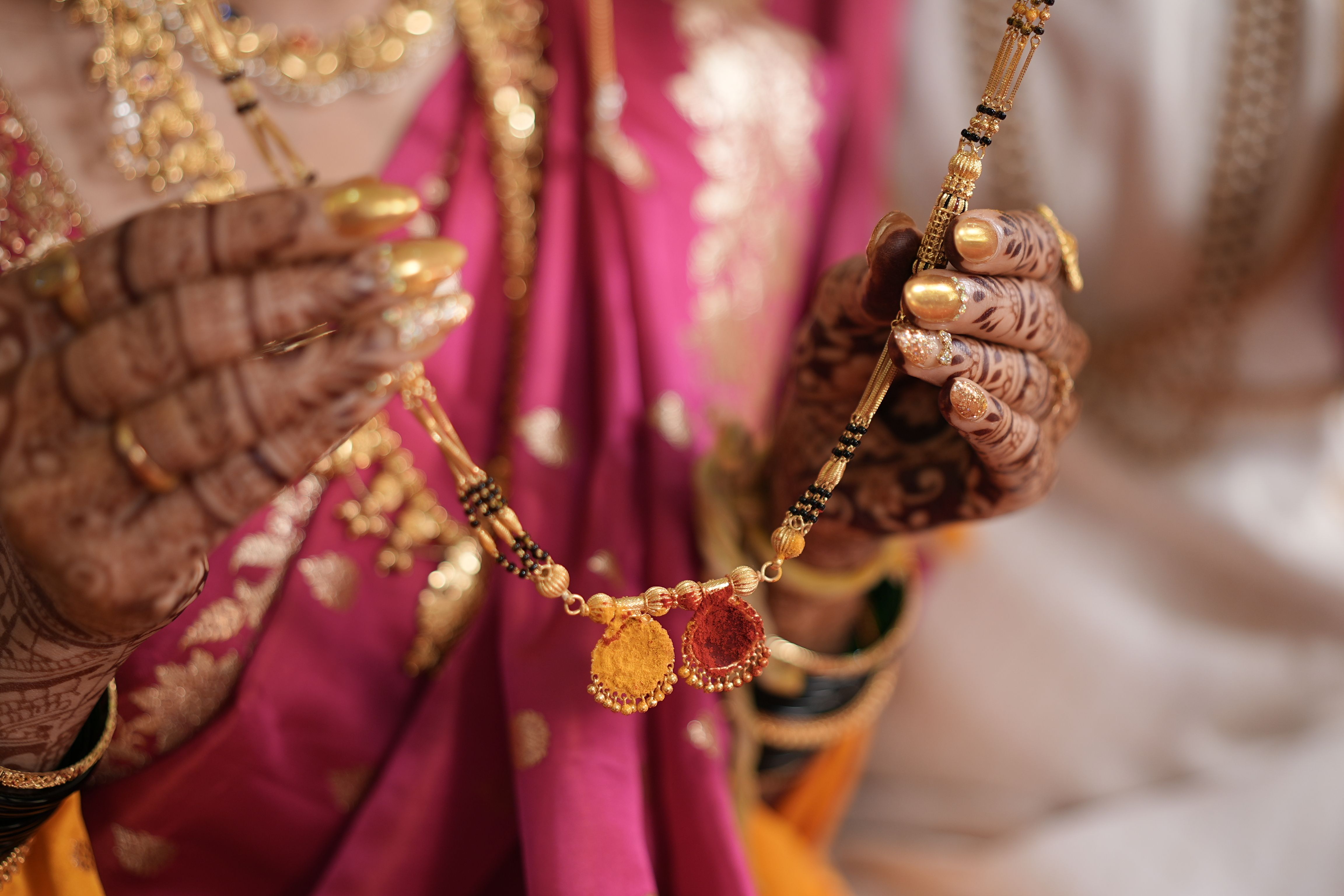 Close-up of a bride showcasing a traditional Indian gold mangalsutra during a wedding ceremony.