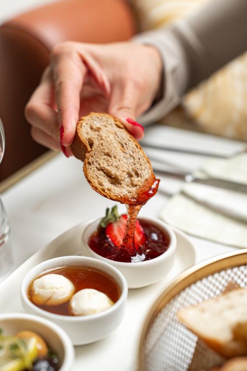 Free A hand dipping whole grain bread into strawberry jam, accompanied by gourmet breakfast dishes. Stock Photo