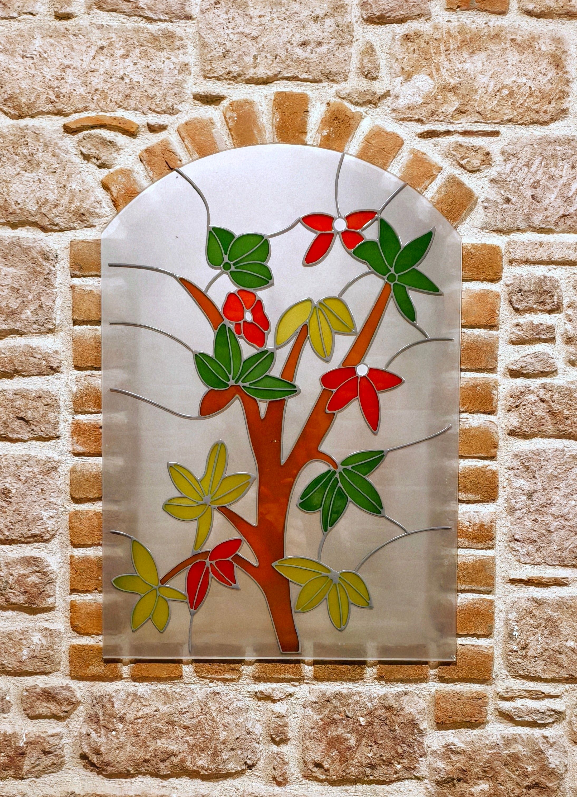 Vibrant stained glass artwork with green, red, and yellow leaves on a brick wall in Balıkesir.