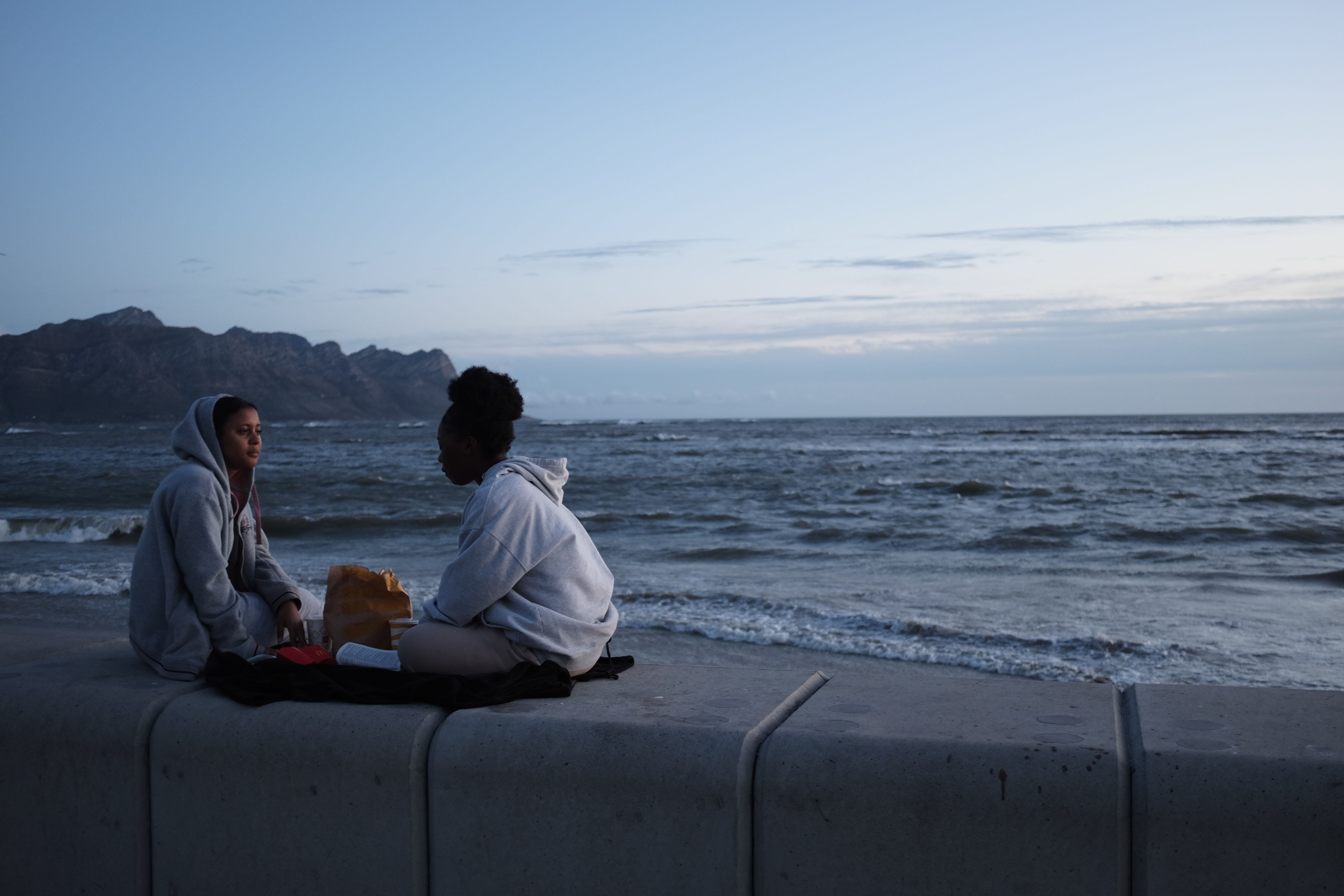 Two friends chat by the ocean during twilight, capturing a serene South African evening.