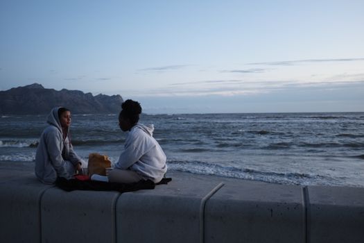 Two friends chat by the ocean during twilight, capturing a serene South African evening.