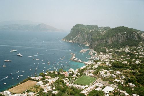 Free Stunning aerial view of Capri's coastline with boats and lush hills, overlooking the marina and harbor. Stock Photo