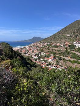 Captivating view of a coastal village in Sardinia surrounded by lush hills and the Mediterranean Sea.
