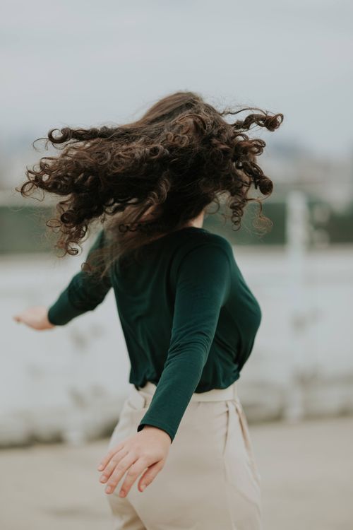 Free Wavy-haired woman in green top spinning joyfully outdoors, expressing freedom and movement. Stock Photo