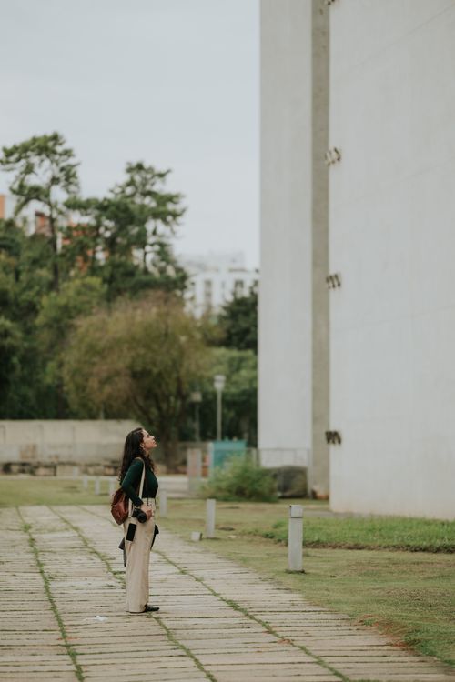 Free A woman stands in an urban park looking at a tall building, conveying curiosity and contemplation. Stock Photo