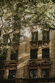 A classic building facade adorned with intricate designs, bathed in sunlight through lush tree branches.