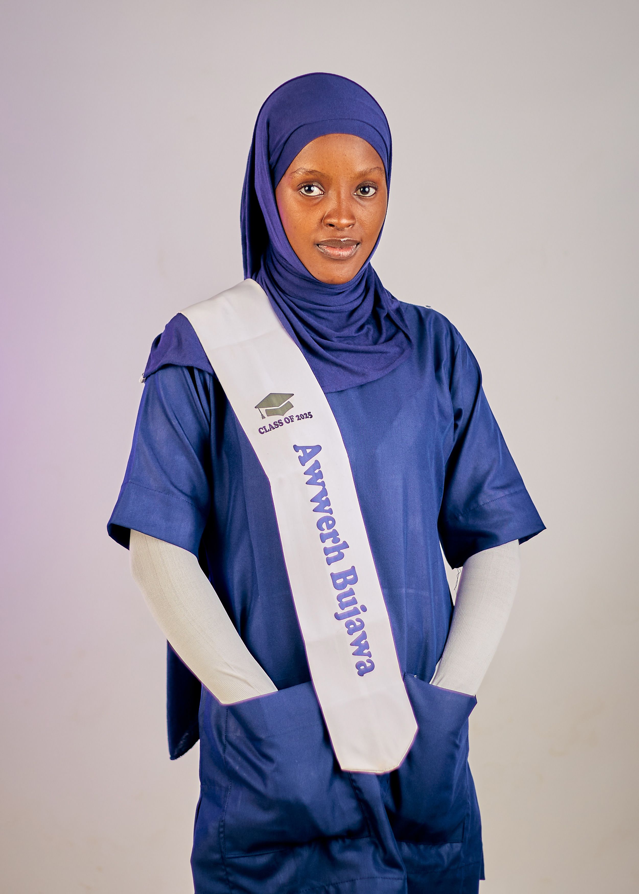 Young woman in hijab and graduation sash posing confidently indoors.