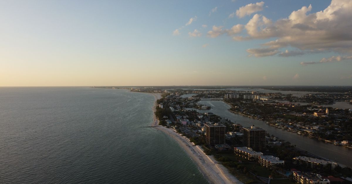 Dramatic aerial view of a coastal city with stunning sunset lighting and expansive ocean vistas.