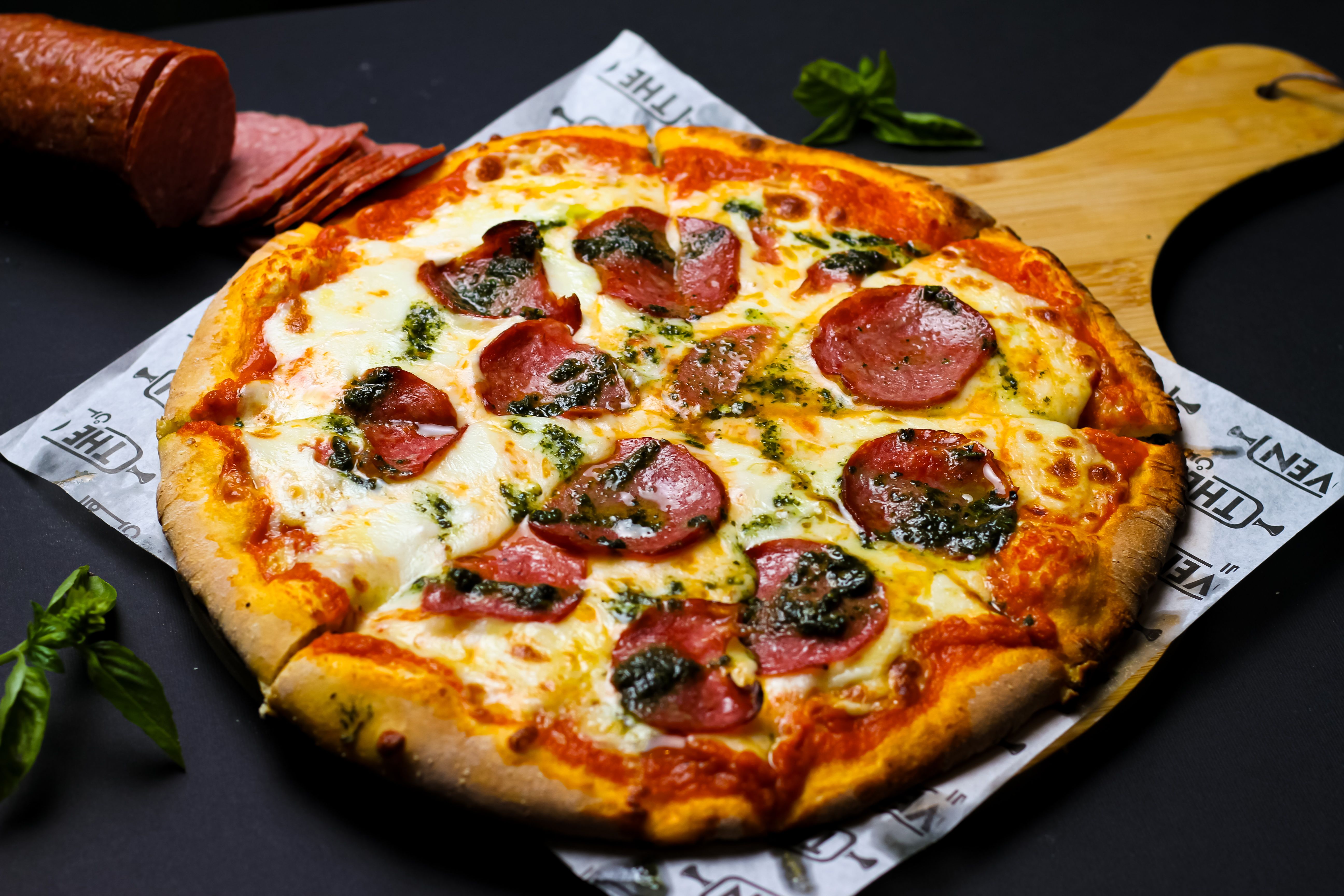 Freshly baked pepperoni pizza with basil on a wooden serving board.