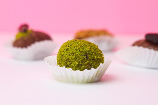 Close-up of colorful assorted truffles with pistachio, featuring a pink background.