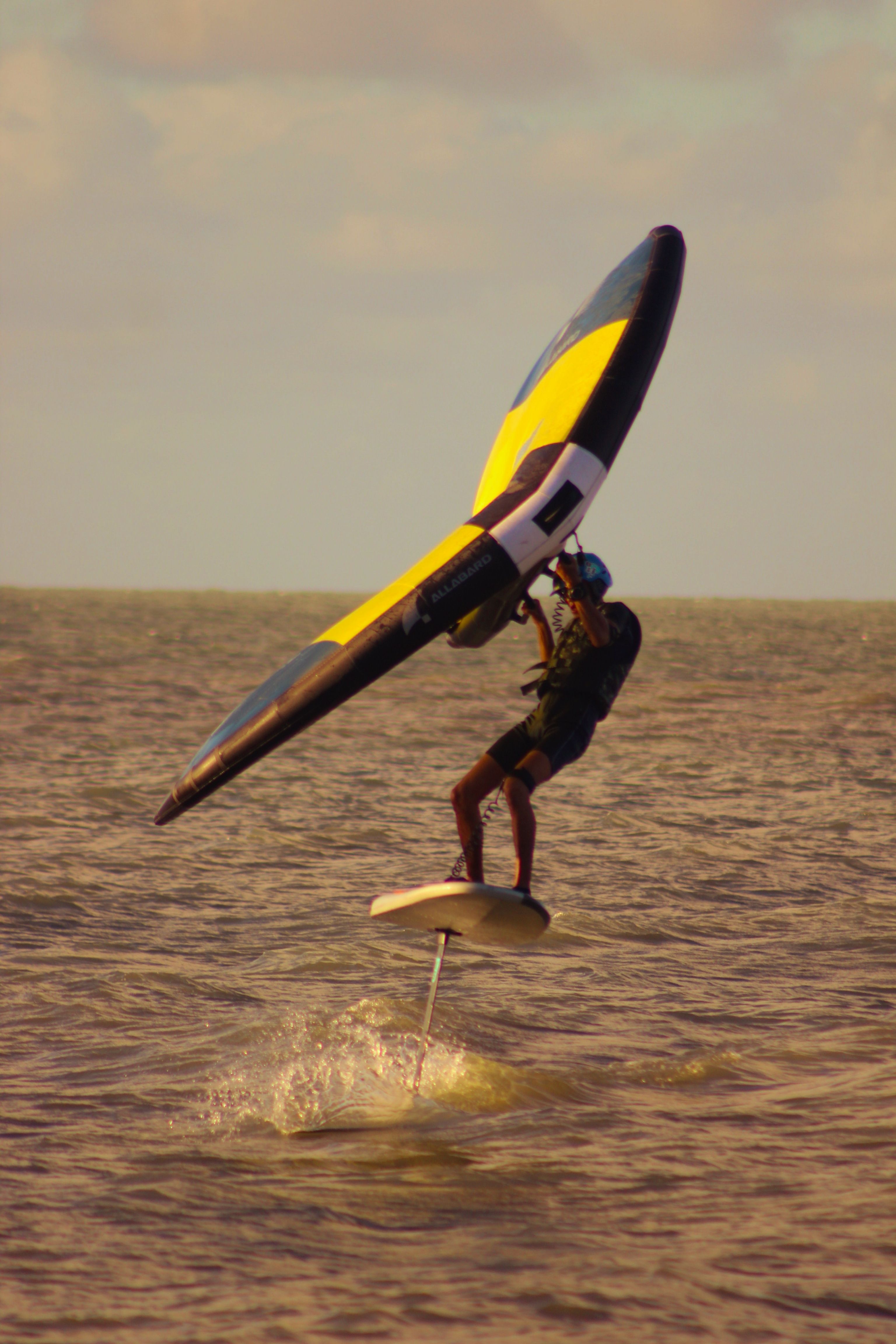 Adult male enjoying wing foiling on a sunny day, showcasing water sport skills.