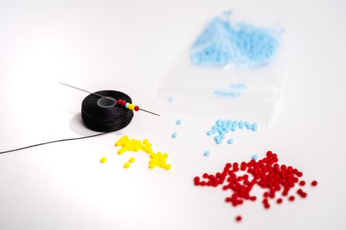 Free Close-up of colorful beads with a needle and thread on a white surface, ideal for craft and DIY projects. Stock Photo