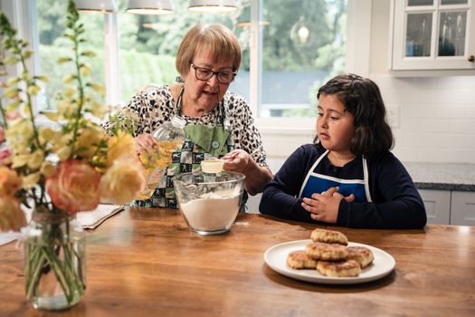 An intimate kitchen scene of a grandmother teaching her granddaughter how to bake traditional bannock.