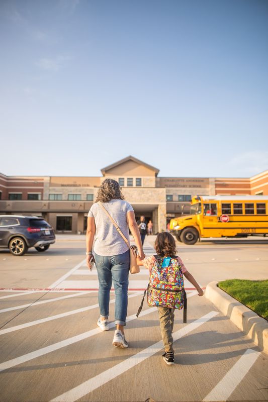 A mother walking her daughter to school, holding hands