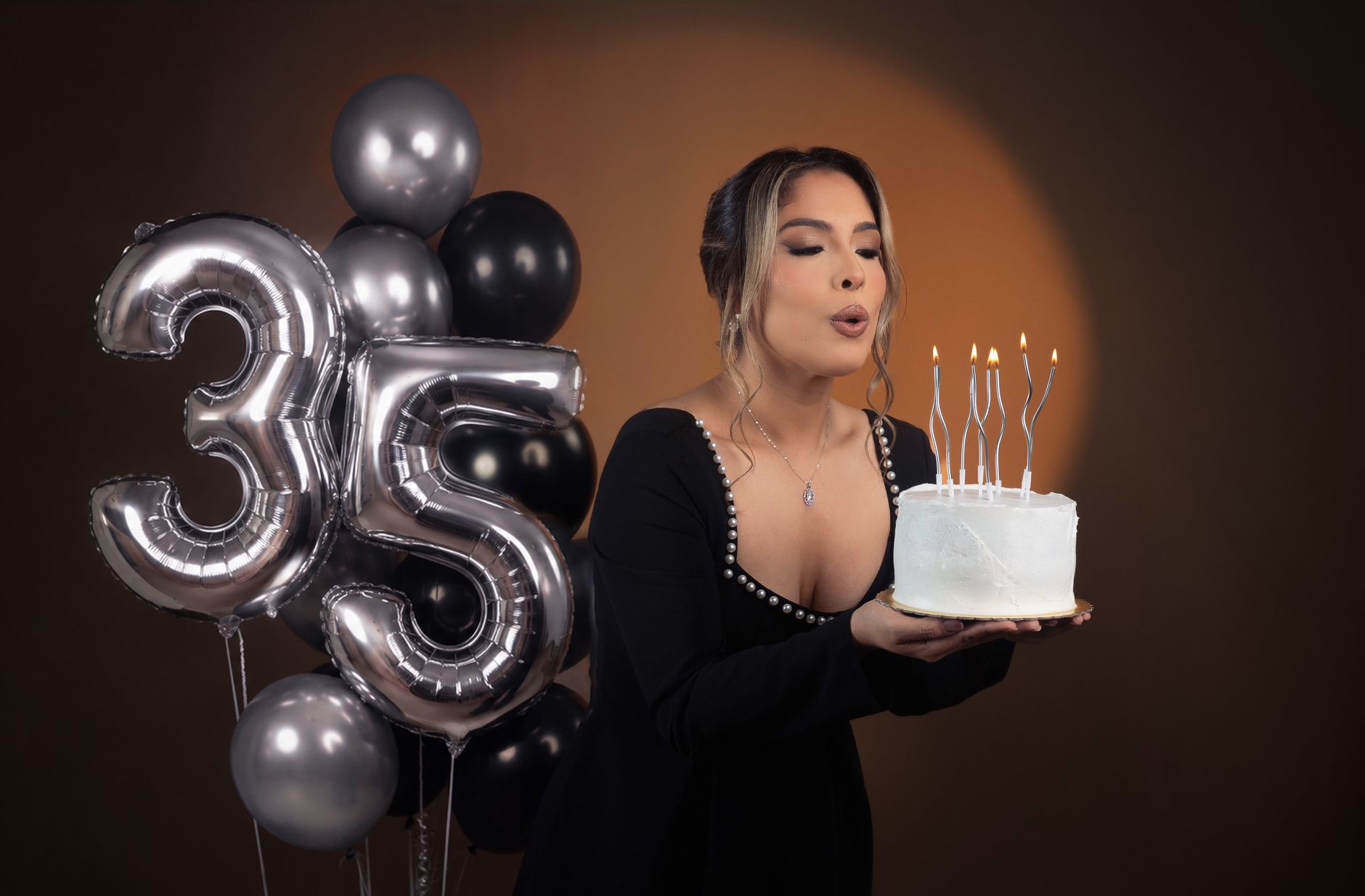 Woman celebrating her 35th birthday with candles on a cake and balloons, conveying joy and elegance.