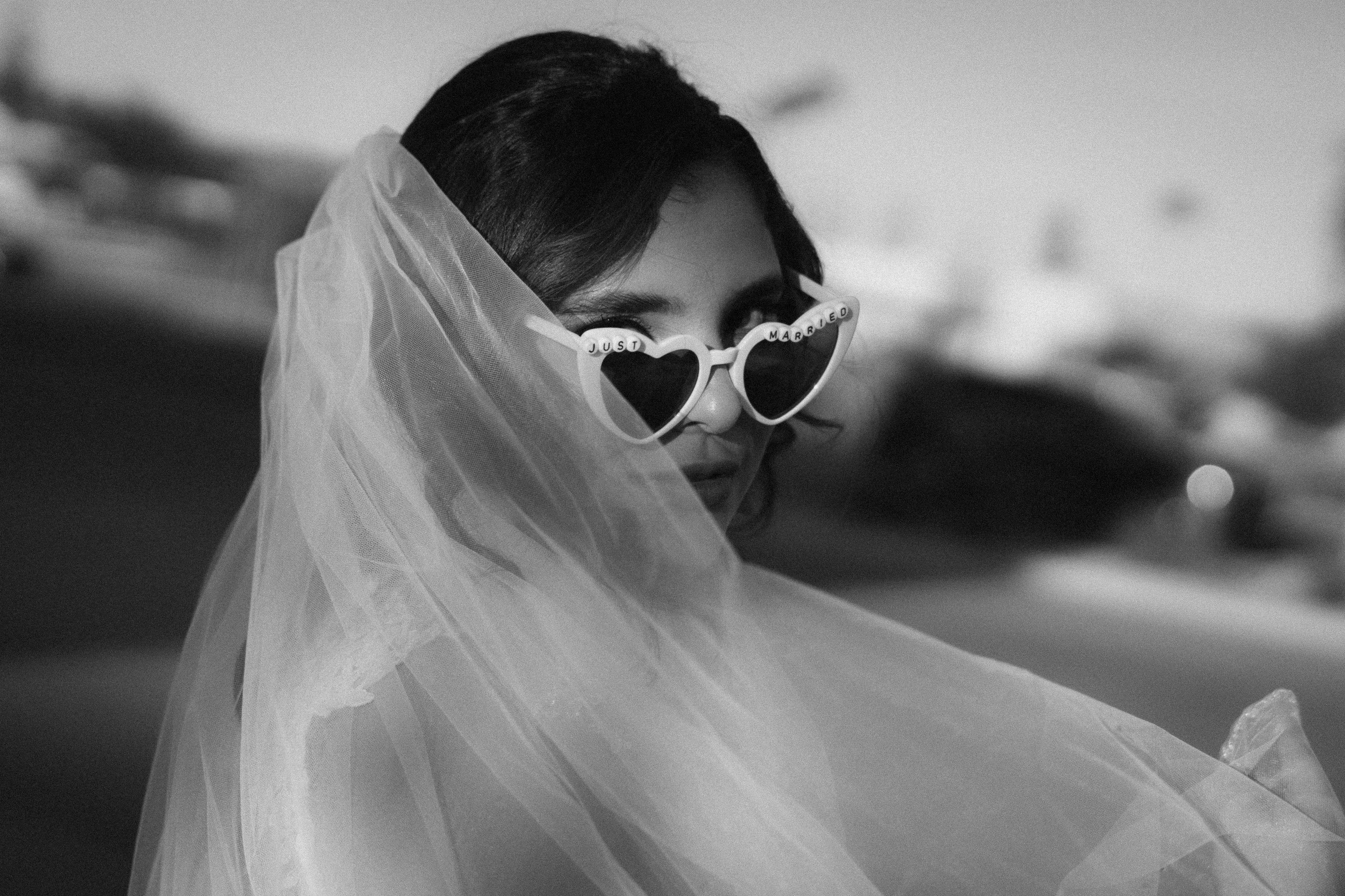 Elegant woman in bridal veil wearing sunglasses outdoors, captured in artistic black and white.