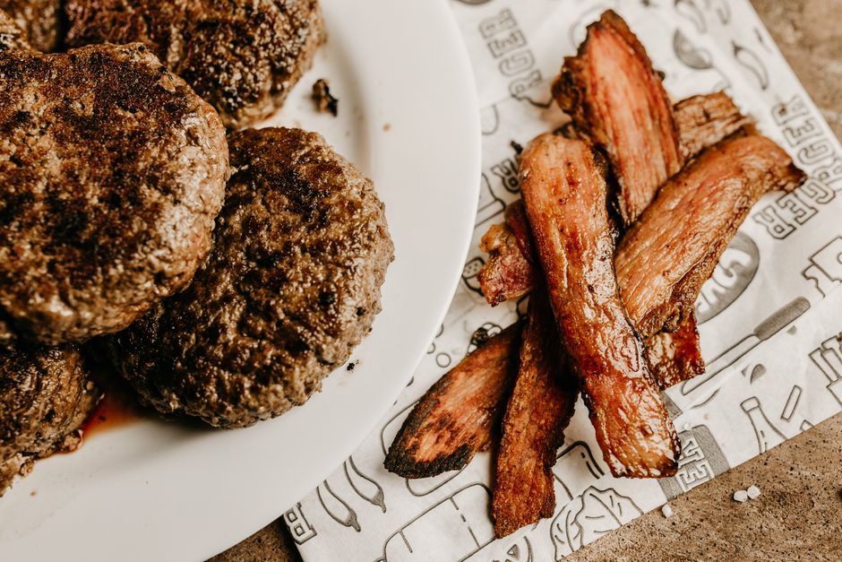 Rows of crisped thick-cut bacon strips cooling on a wire rack set inside a rimmed baking sheet, with visible rendered fat and deep golden-brown edges.