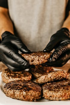 Close-up of hands cooking beef patties, showing culinary skills and delicious food preparation.