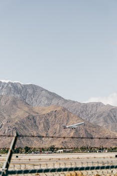 飞机在晴朗的天空和低云下，白天从机场栅栏和高高的粗糙坐骑之间的道路起飞