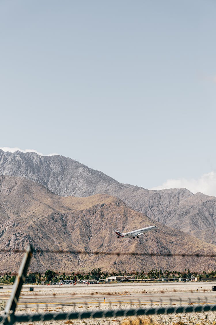 Airplane Taking Off From Runway Near Mountains Under Serene Sky