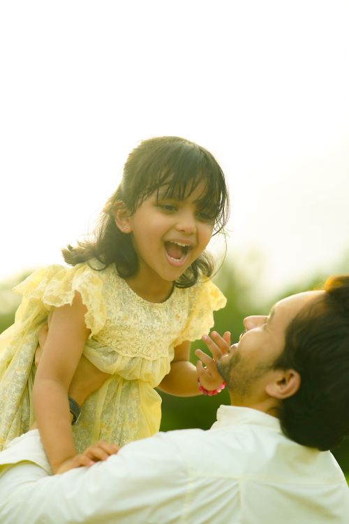 Free A joyful father lifts his daughter in the air, capturing a moment of happiness in the sunlight. Stock Photo