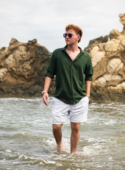Young man strolling through shallow water by rocky shores in Puerto Escondido, Córdoba, Colombia.