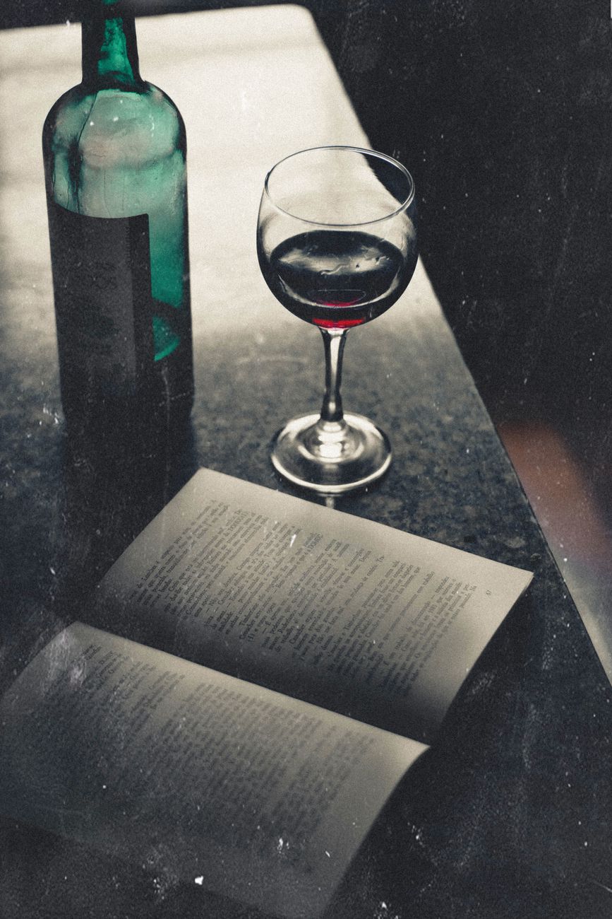 Artistic still life showcasing a vintage wine bottle, glass, and book in a dimly lit setting.