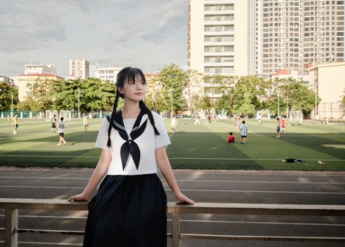 Free A teenager in a sailor-style school uniform stands by a sports field on a sunny day. Stock Photo